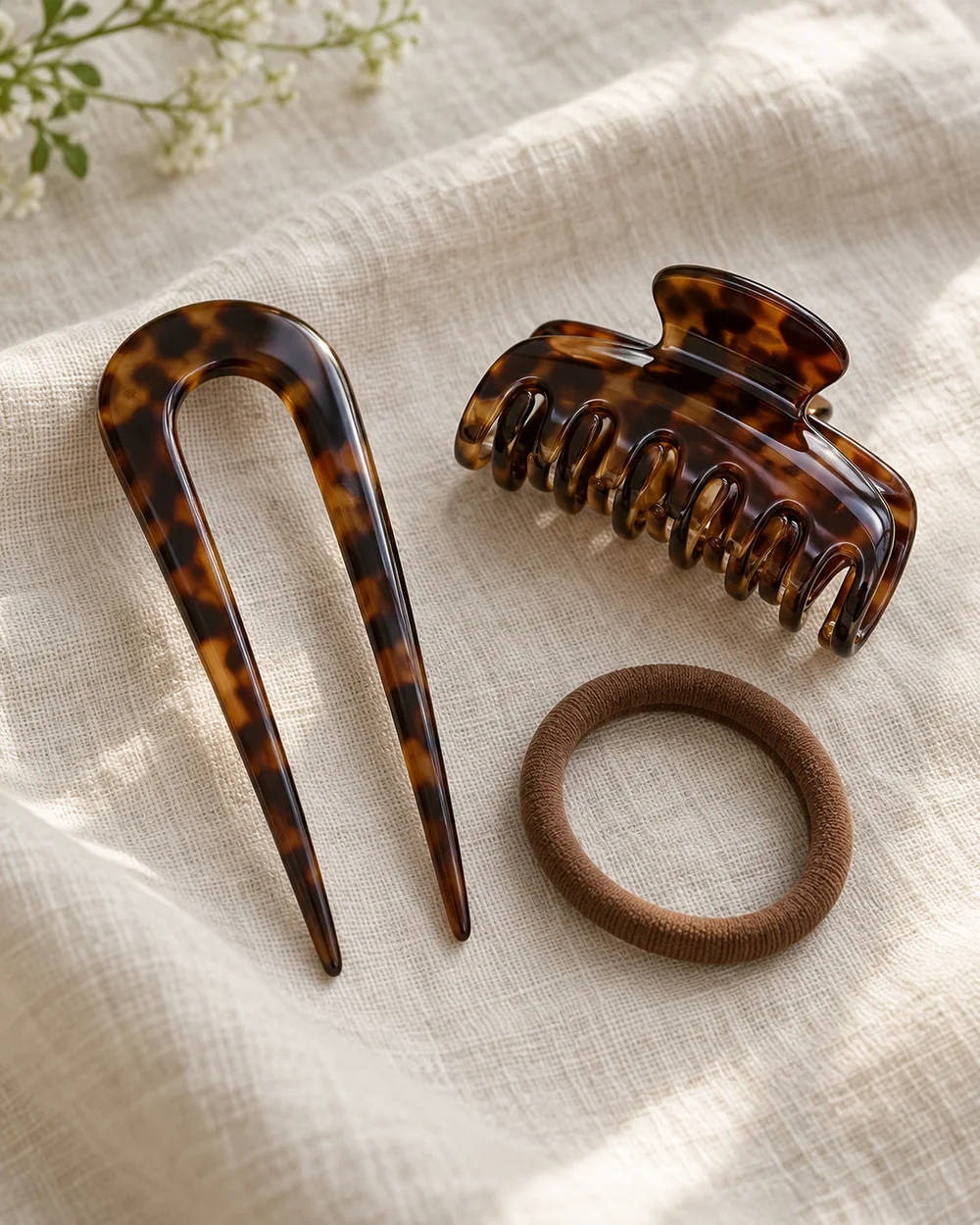 Smooth tortoiseshell U-shaped French hair pin, brown claw clip and soft brown hair tie on linen.