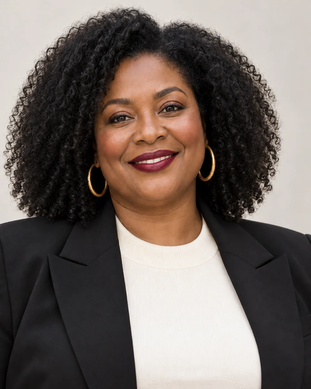 A fictional mature woman with deep warm brown skin, dark curls and full facial proportions wearing contained copper lids and a clear burgundy satin lip with black tailoring and cream knit.
