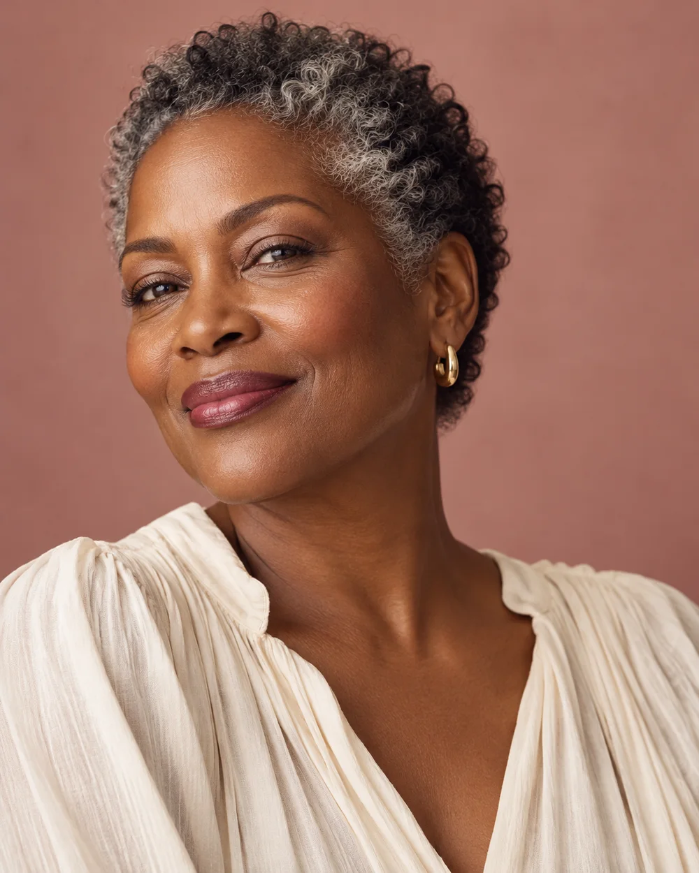 A woman with deep brown skin, short salt-and-pepper curls and a softly defined berry-plum lip.