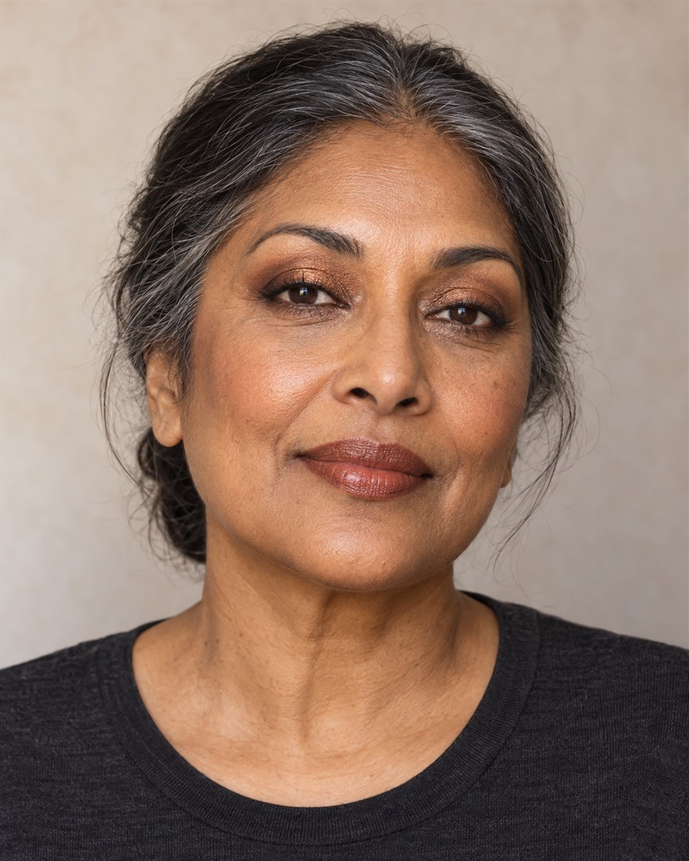 A woman with medium-deep brown skin and silver-streaked dark hair wears bronze lids, softly shaded outer eyes and a warm brown lip.