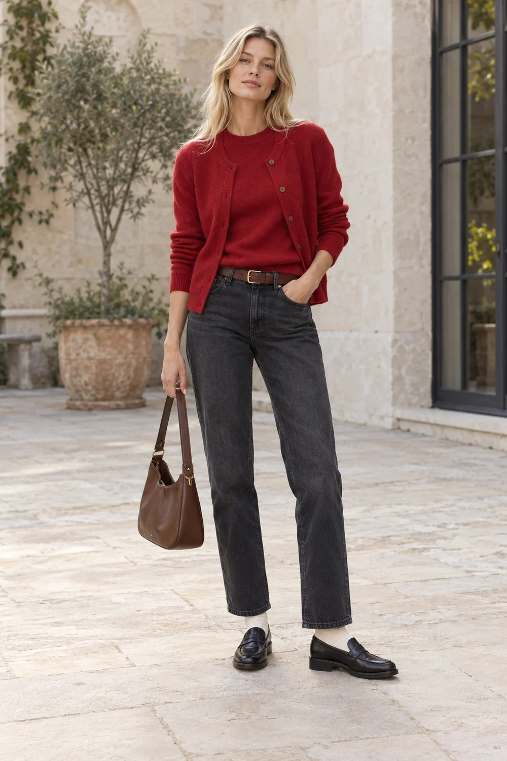 A fictional woman in layered red knits, charcoal jeans, black loafers, ivory socks and brown belt and bag.