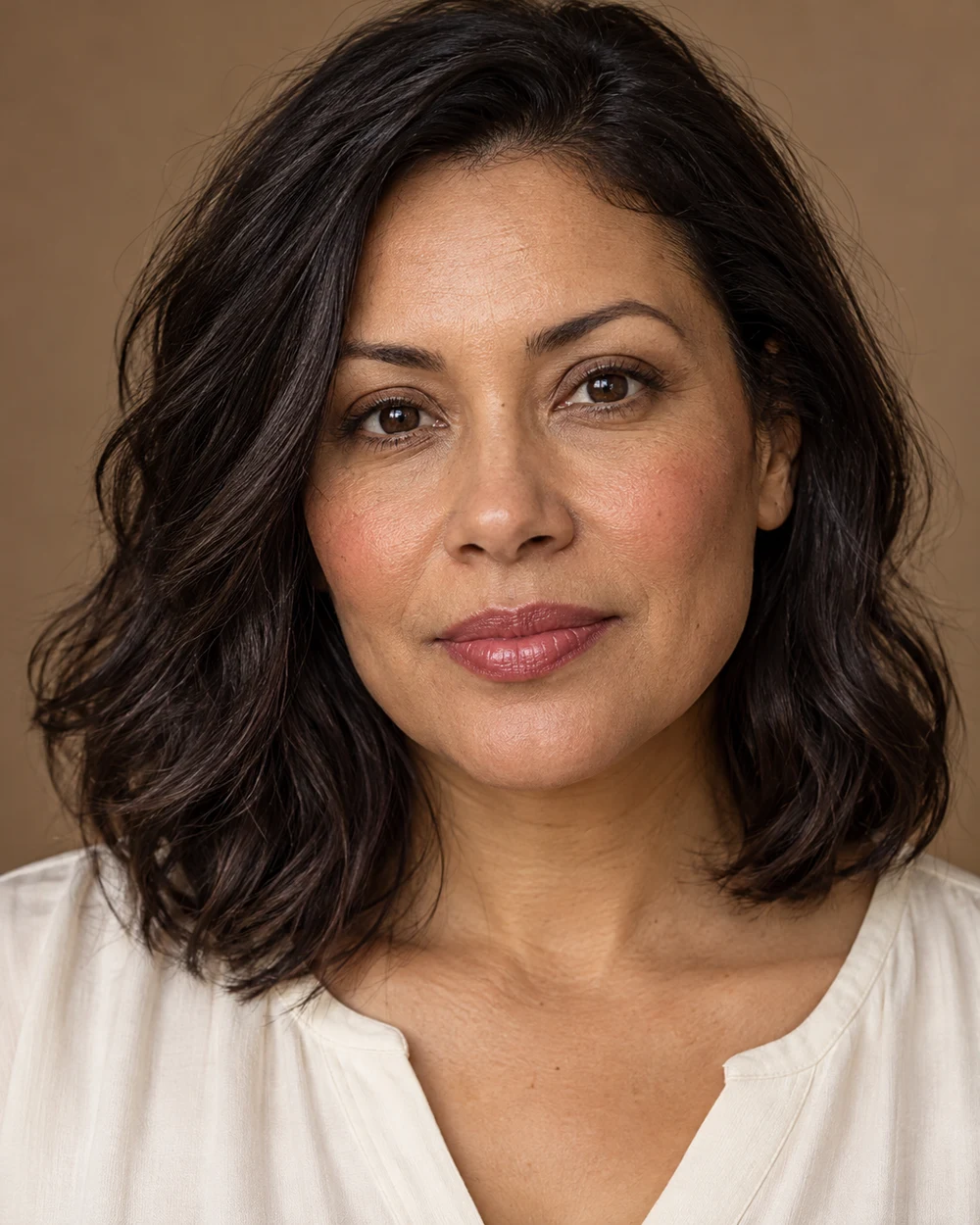 A fictional adult with medium neutral-brown skin, softly coordinated rose cheek and lip colour and quiet brown lashes beside a cream top.
