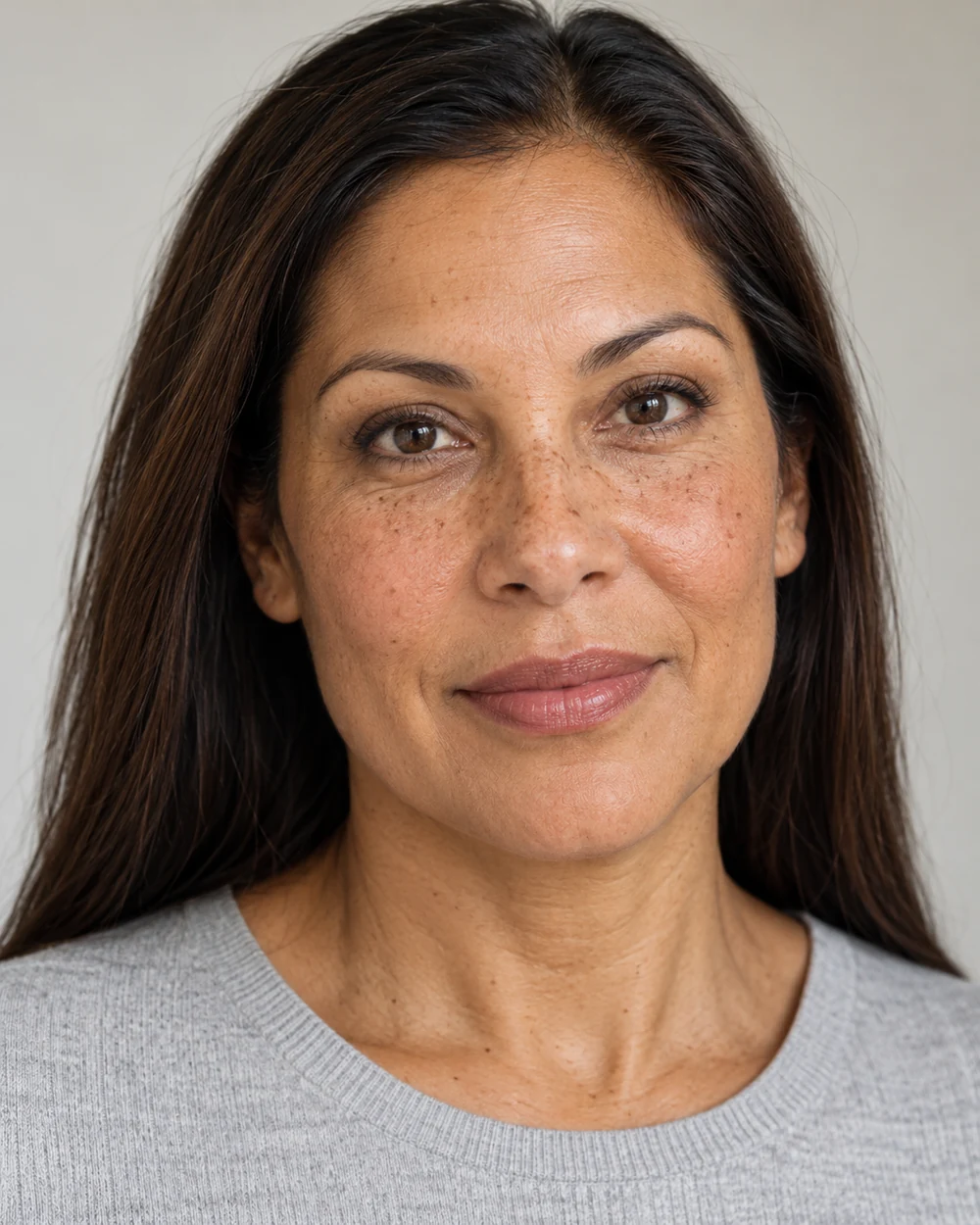 A fictional woman with light-medium warm brown skin, natural freckles and dark hair wearing selective coverage and a defined rose-brown mouth with a pale-grey neckline.
