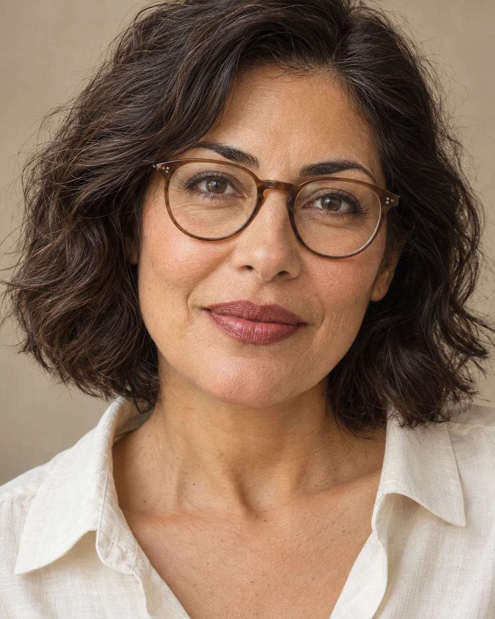 A fictional adult with medium olive skin wearing understated rounded glasses, a contained rose-brown satin lip with a deliberate edge and quiet eye makeup.