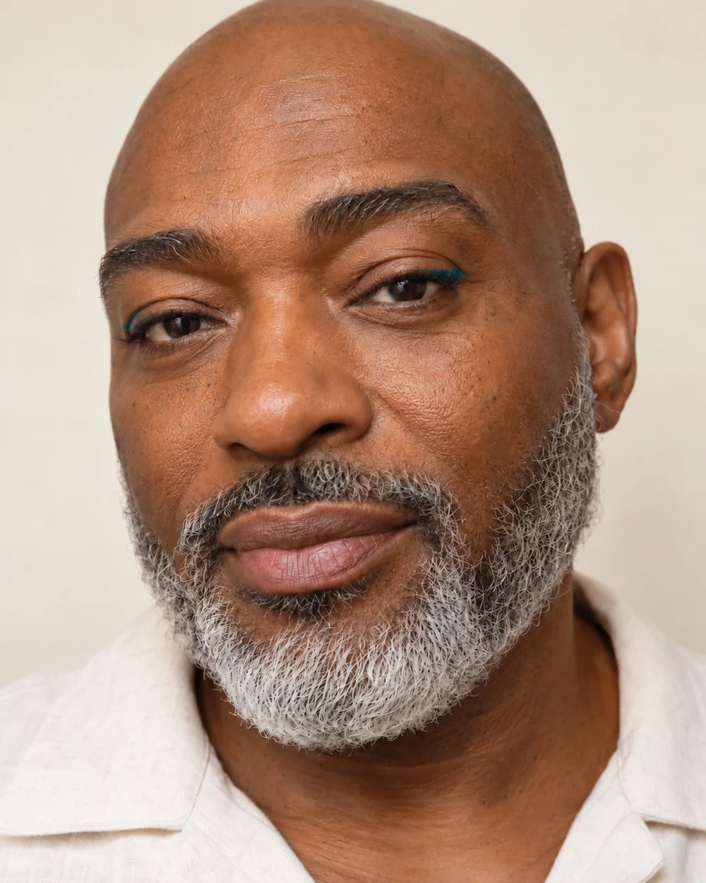 An adult with medium-deep warm brown skin, natural skin texture and a contained teal upper-lash line.