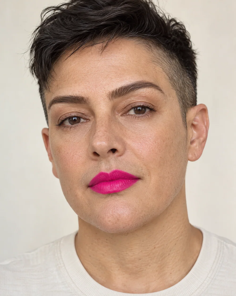 An adult with light-medium neutral skin, natural skin texture and a hot pink mouth and a softly brushed brow.