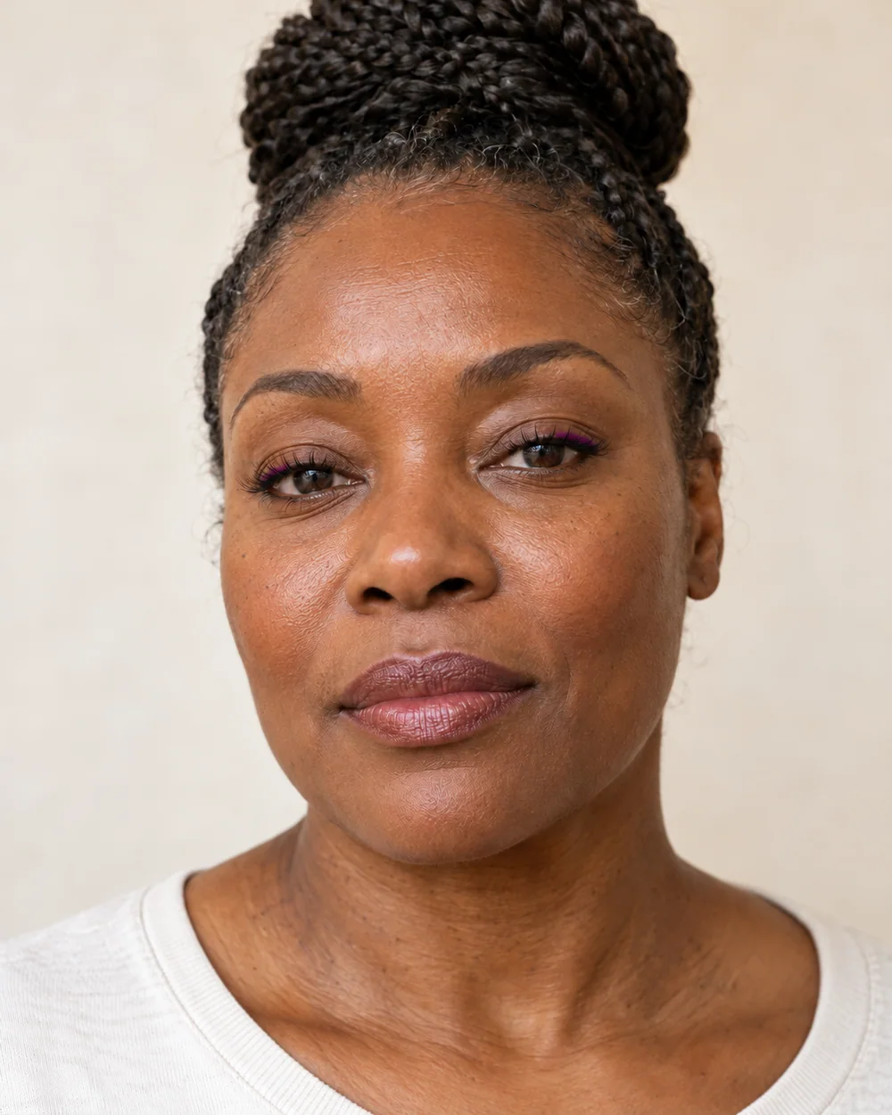 An adult with deep brown skin, natural skin texture and a bright plum lash line.