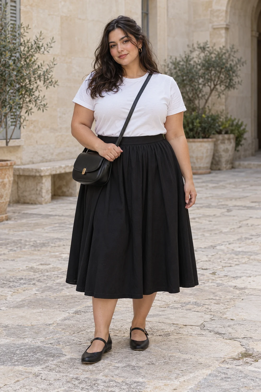 A fictional woman in white tee, black A-line midi skirt, black flat Mary Janes and black crossbody bag.