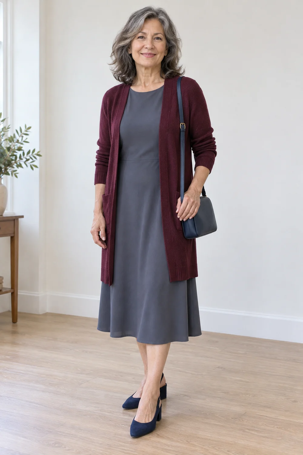 A petite fictional adult in a slate opaque midi dress, burgundy longline cardigan, navy block-heel slingbacks and a compact dark bag, shown full length.