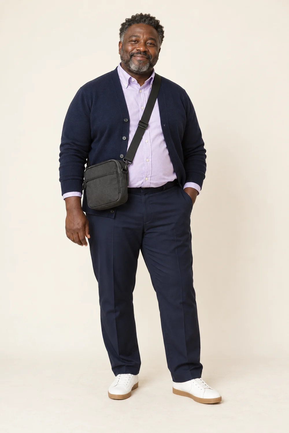 Full-length short plus-size adult man in navy trousers, lilac Oxford shirt, navy cardigan, white gum-sole trainers and charcoal crossbody bag.
