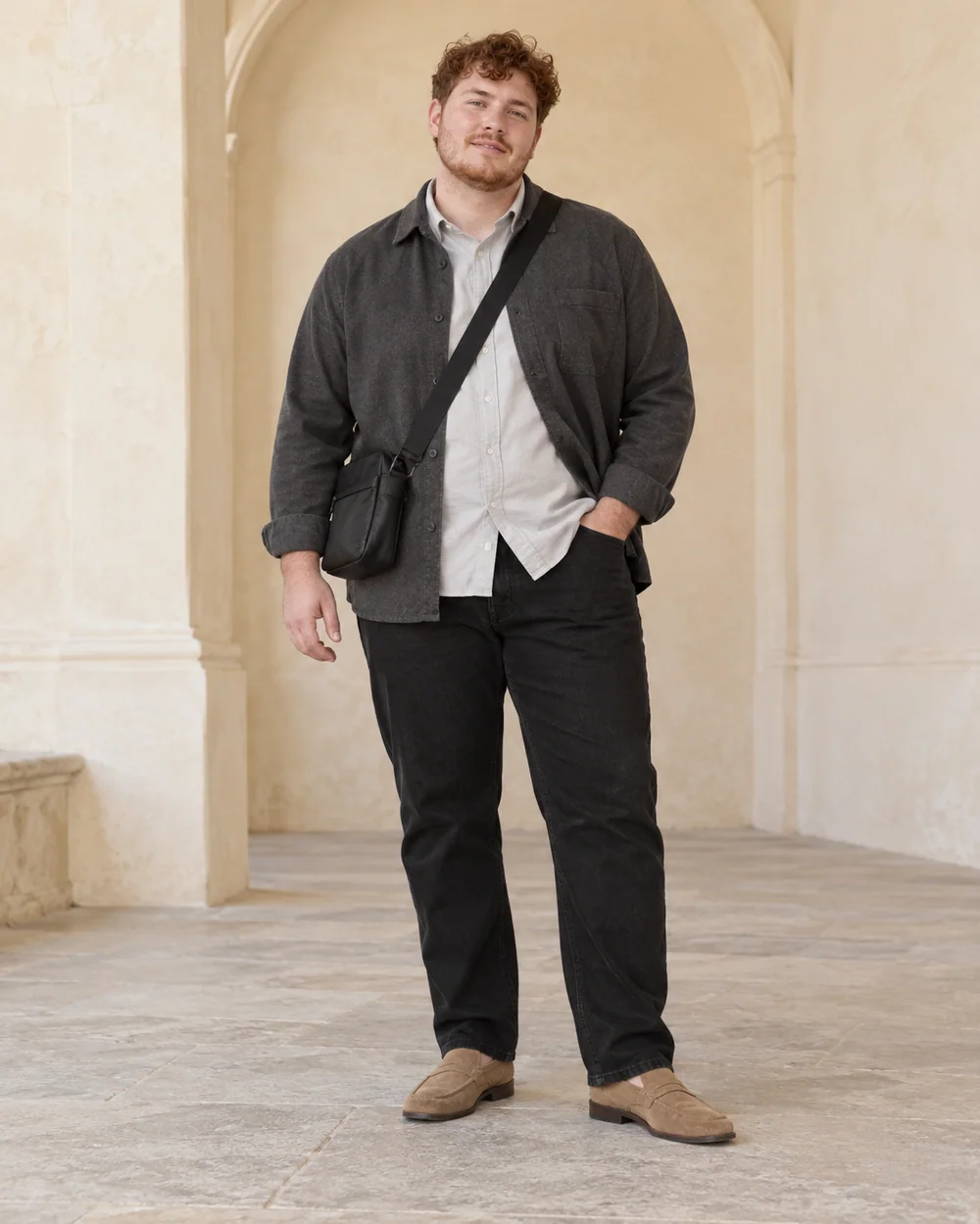 A full-length adult man with fair cool skin wearing Black straight jeans, stone Oxford shirt, Charcoal soft overshirt and Tan suede-look loafers, with a small dark crossbody bag; both complete shoes are visible.
