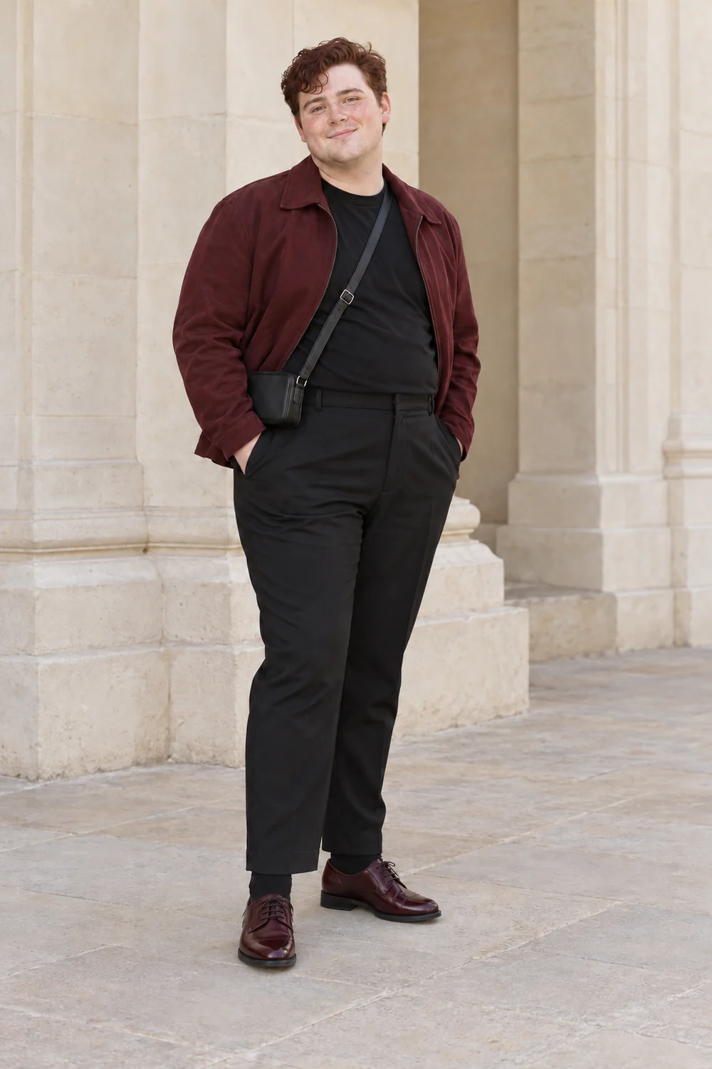 A petite plus-size fictional adult man in a black tee and tailored trousers, burgundy soft jacket, burgundy Derby shoes with black socks and a dark compact bag, shown full length.
